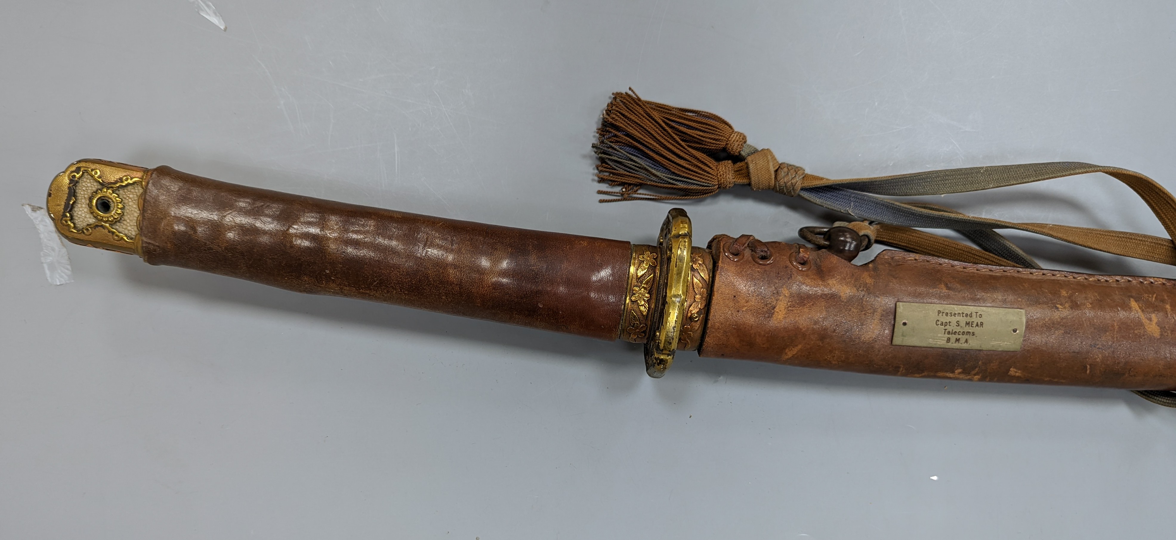 A Japanese Katana with leather covered sheath, plaque reading ‘Presented to Capt. S. Mear Telecoms B.M.A’ 93 cms long.